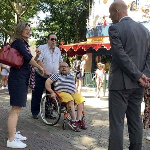 Man in rolstoel en begeleider bezoeken pretpark
