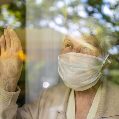 Oude vrouw met mondkapje, achter het raam