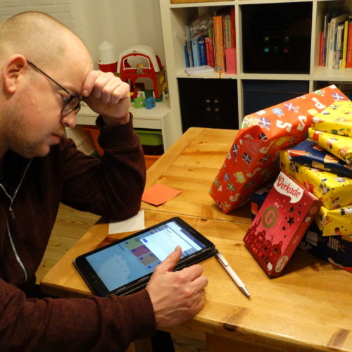 Wolter probeert op tablet online te bestellen, op tafel ligt een stapel sintcadeautjes