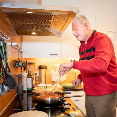 Een bewoner van Bartiméus roert staat in een keuken in een pan te roeren.